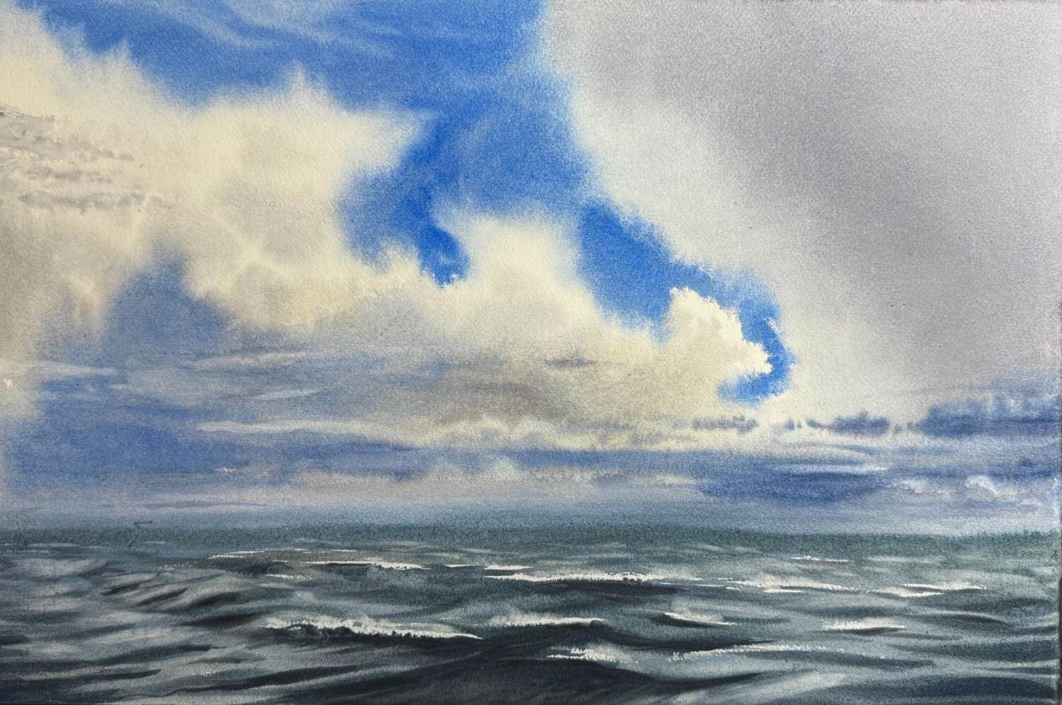 Large white clouds over a dark sea with blue openings in the sky.